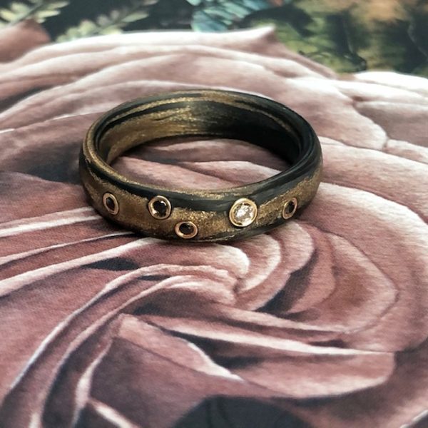 Carbon Bronze Ring von SCHWAB mit naturfarbenen und schwarzen Brillanten in Gelbgold gefasst, Ring liegend