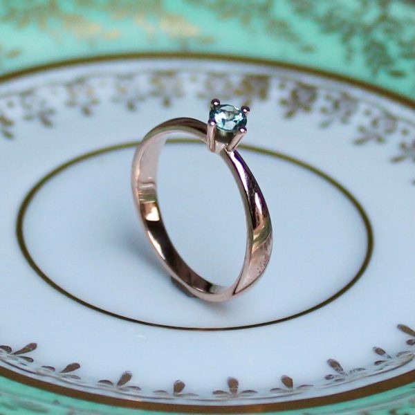 Wunderschöner Rosegold Ring mit hellgrünem Safir auf Porzellan stehend